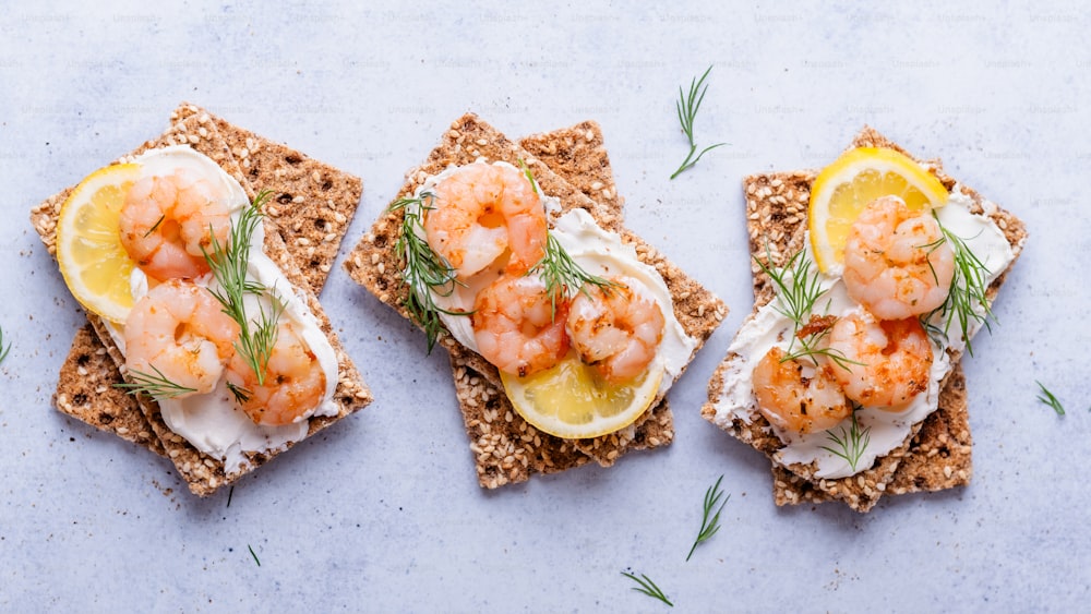 three crackers with crackers topped with shrimp and lemon slices