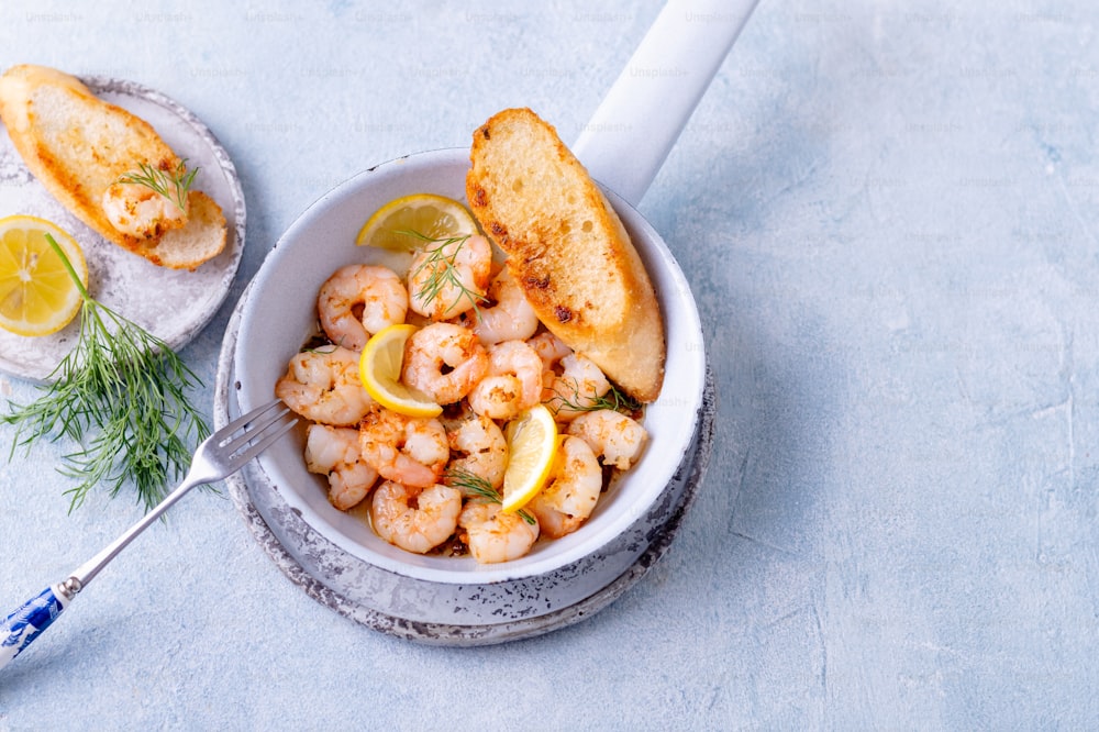 a bowl of shrimp with bread and lemon wedges