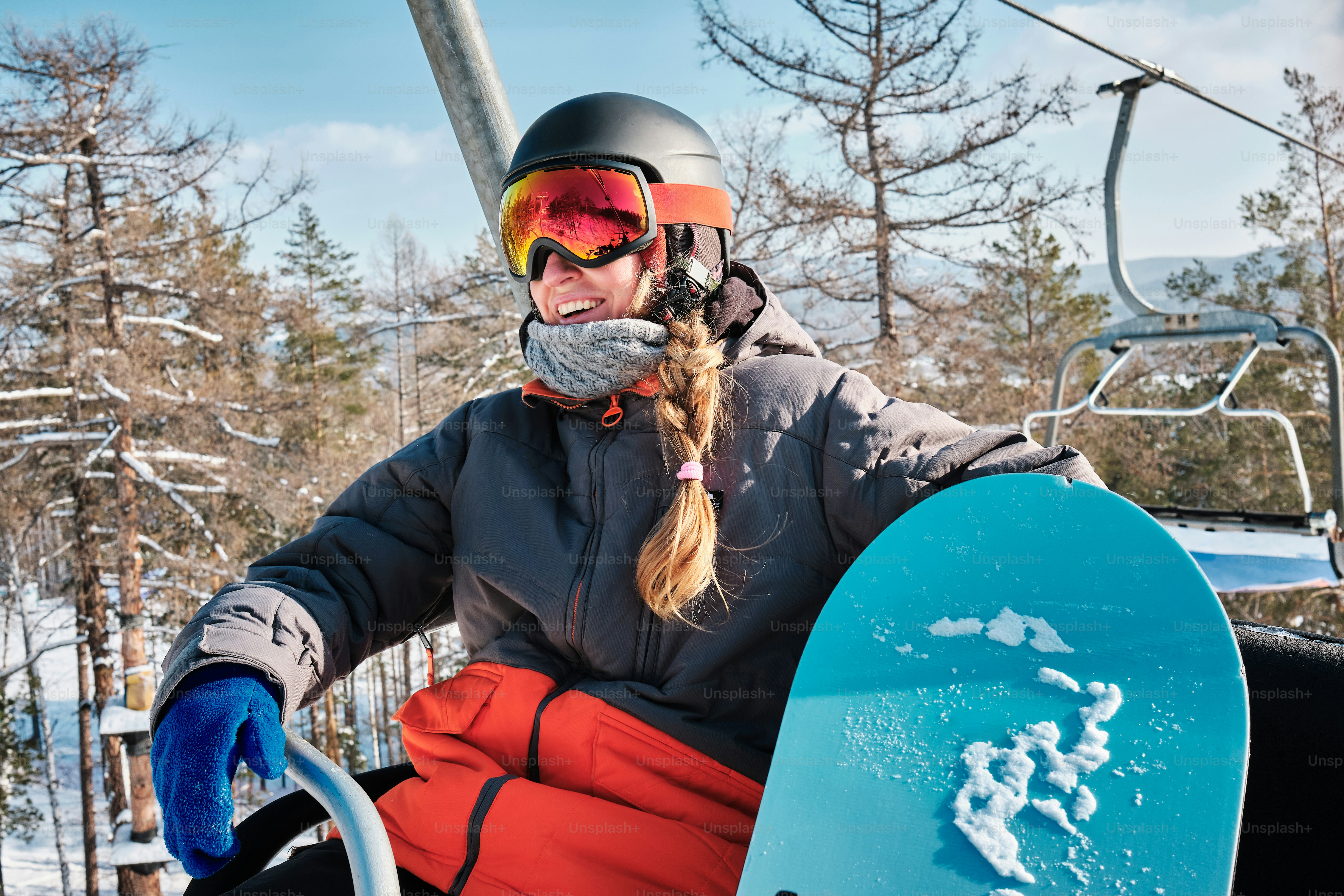 una mujer montada en un telesilla sosteniendo una tabla de snowboard