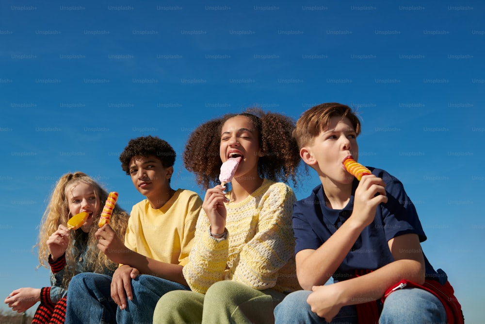a group of children sitting on a bench eating ice cream