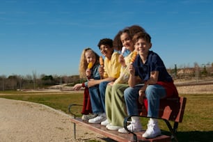 un grupo de niños sentados en un banco comiendo helado