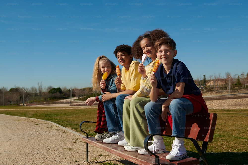 a group of kids sitting on a bench eating ice cream