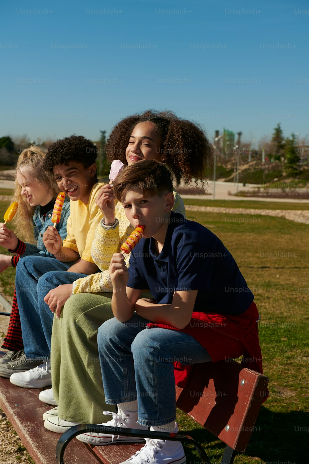 a group of people sitting on a bench eating corn on the cob