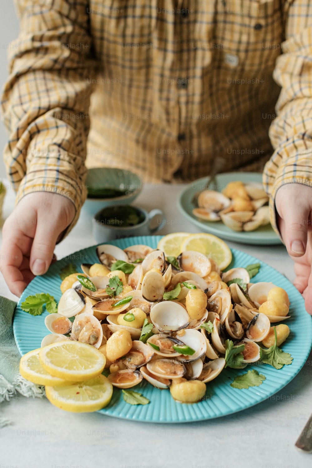a person holding a plate of clams on a table