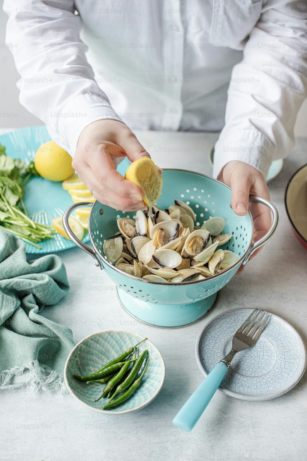 a person is adding a lemon to a bowl of clams