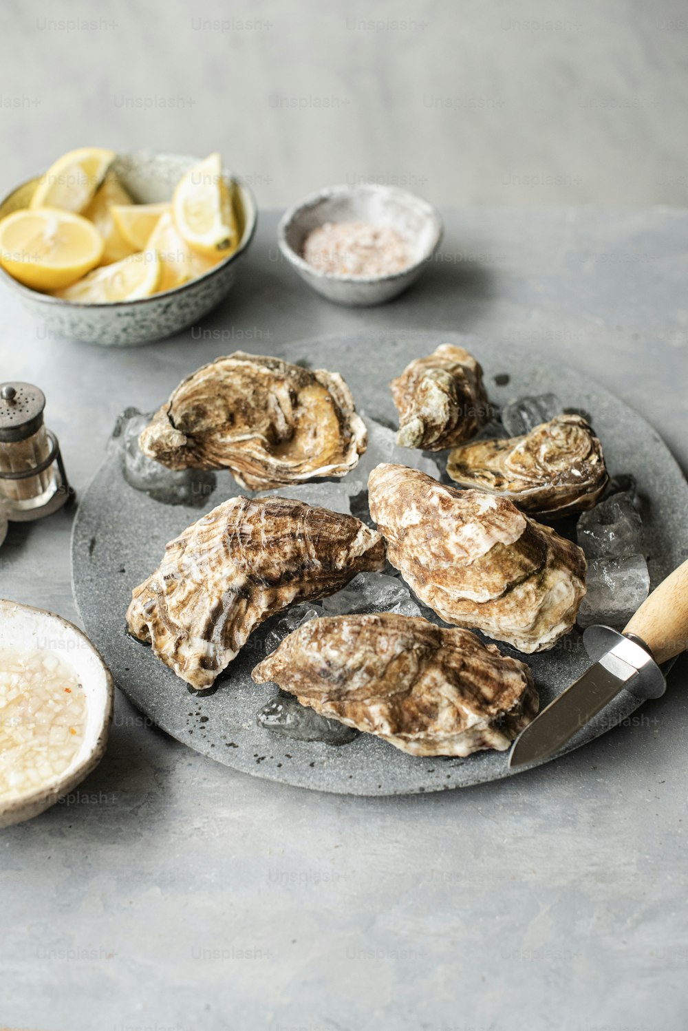 a plate of oysters on a table with lemons and salt