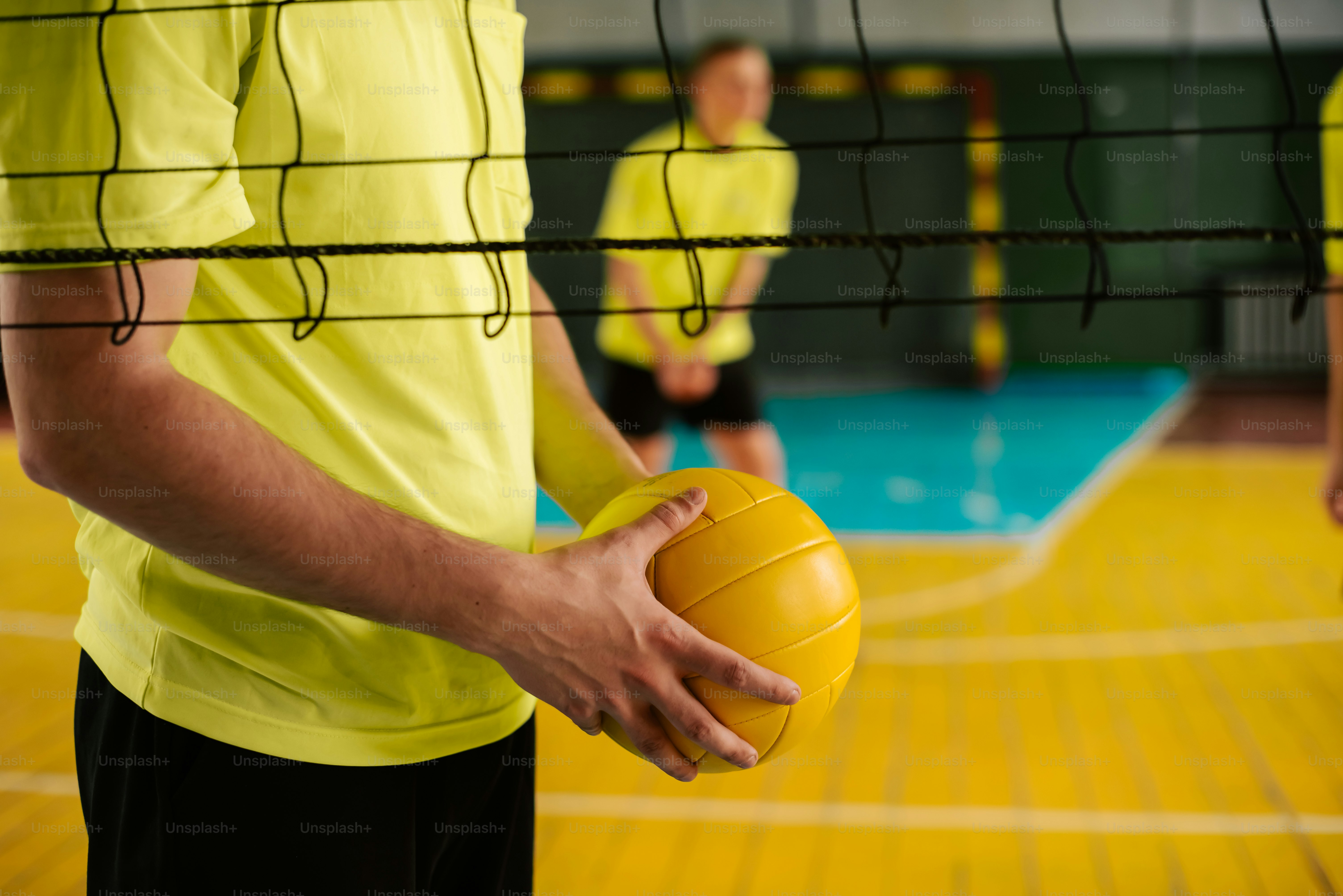 ein Mann hält einen gelben Volleyball auf einem Spielfeld