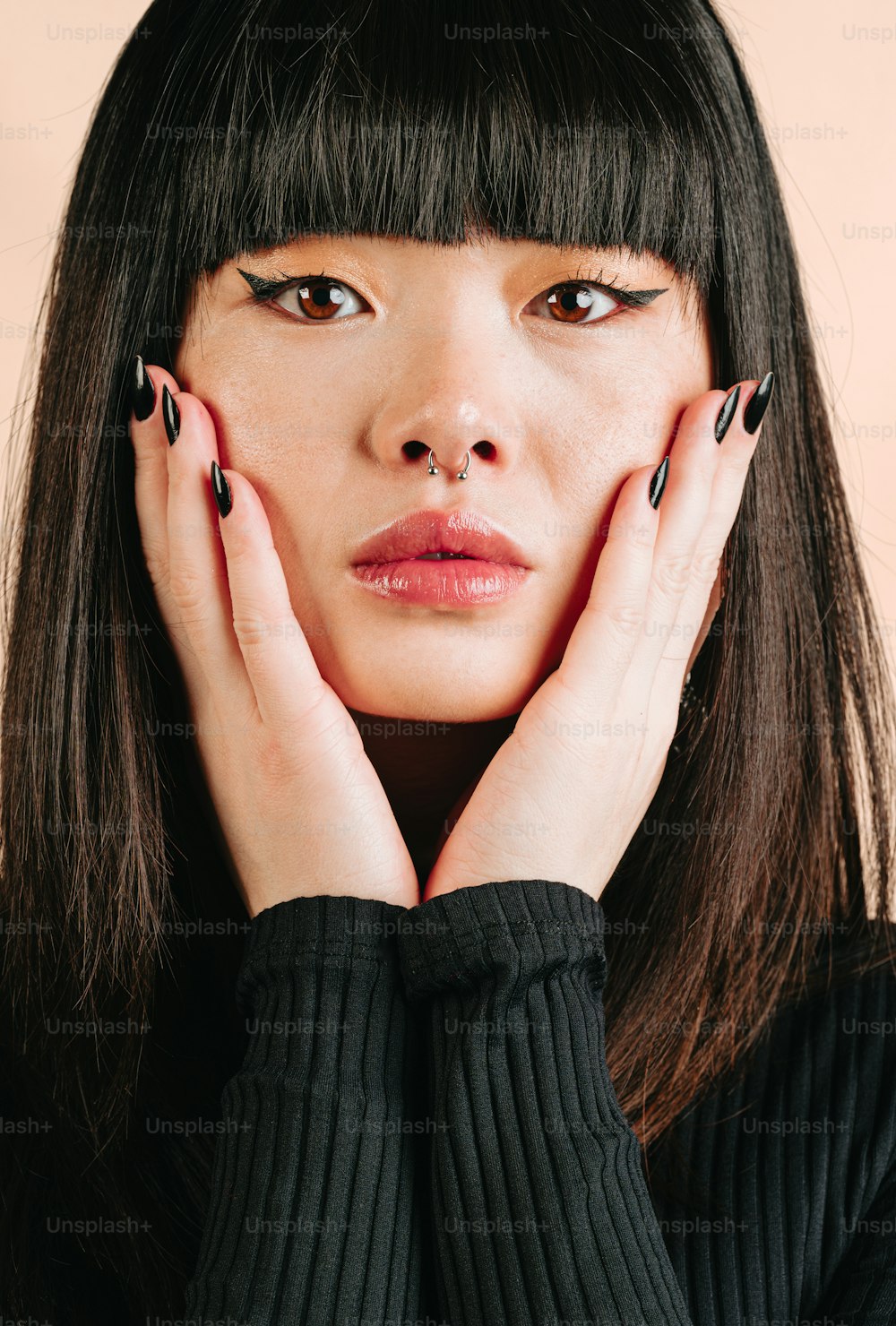 a woman with black nail polish holding her hands to her face