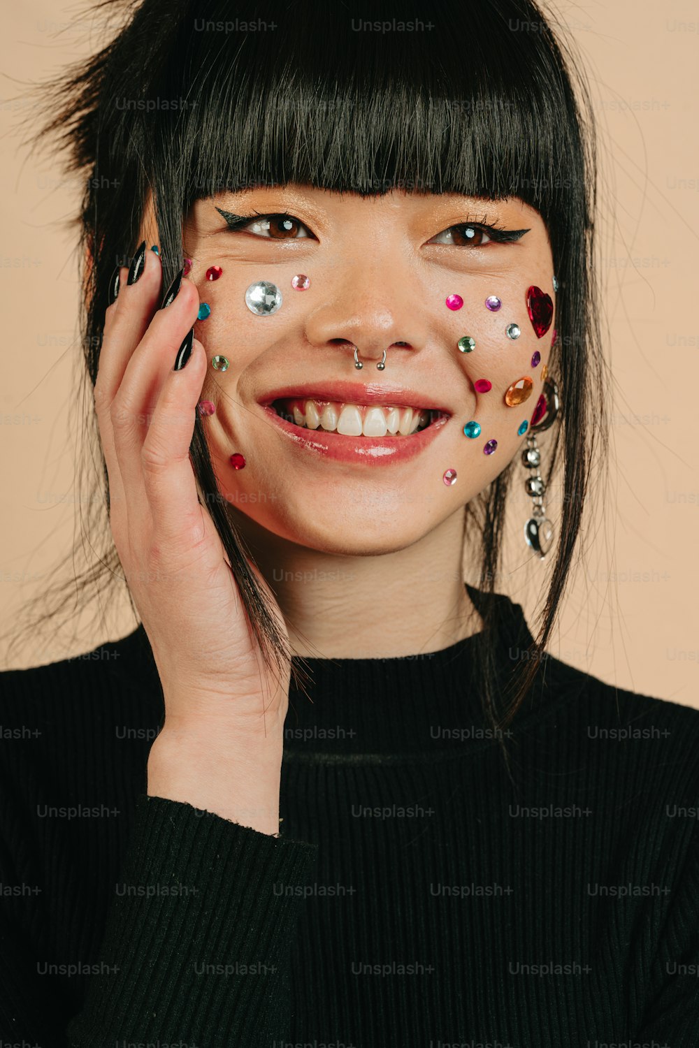 a woman with black hair and a black sweater has colorful nail art on her face
