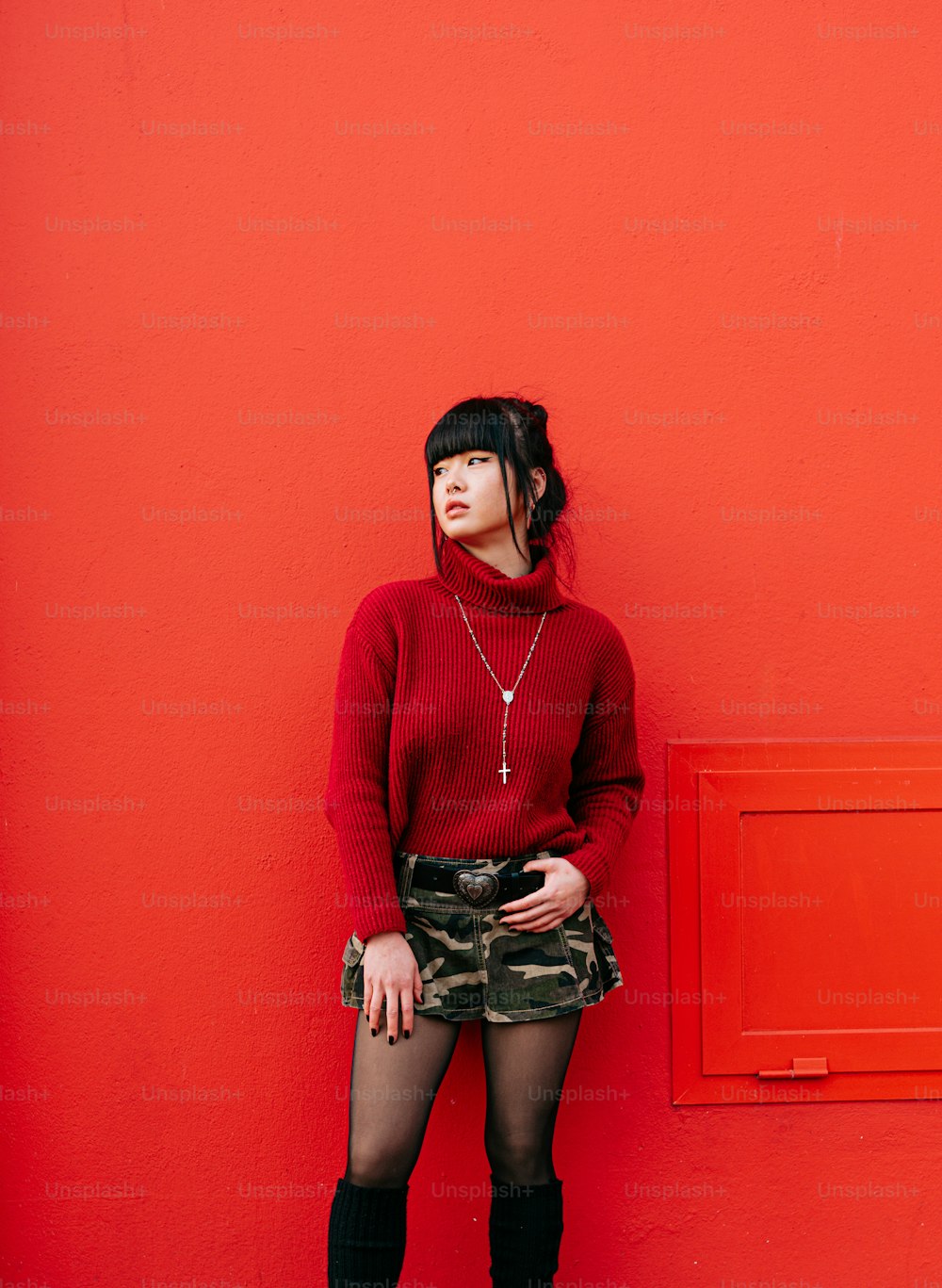 a woman standing against a red wall with her hands in her pockets