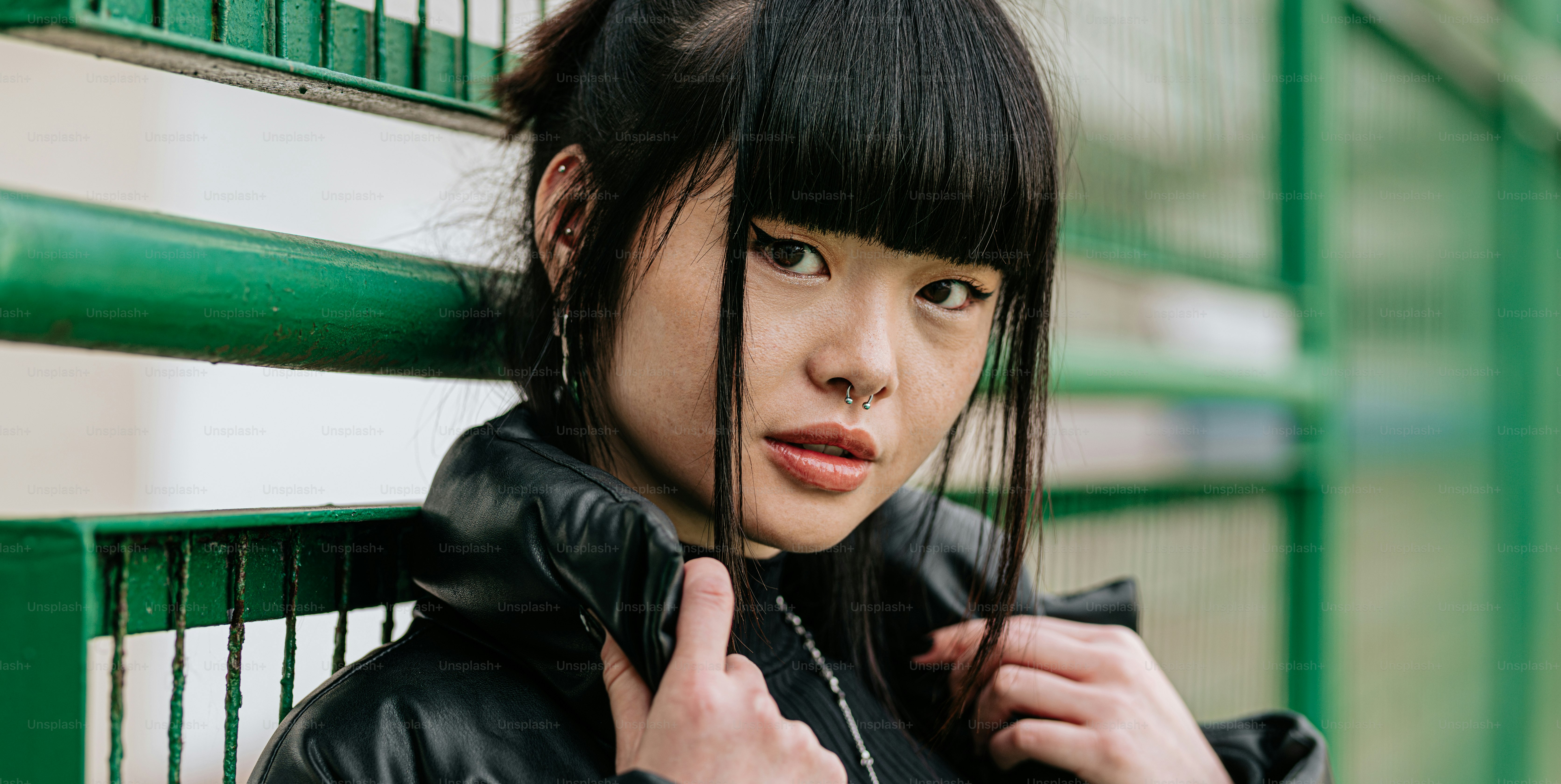 緑の柵にもたれかかっている黒い革ジャンを着た女性