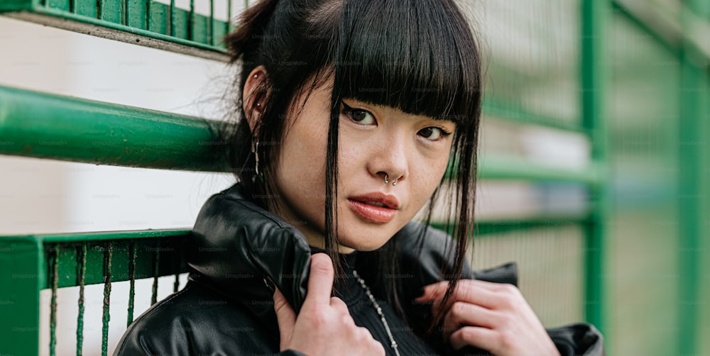 a woman in a black leather jacket leaning against a green fence