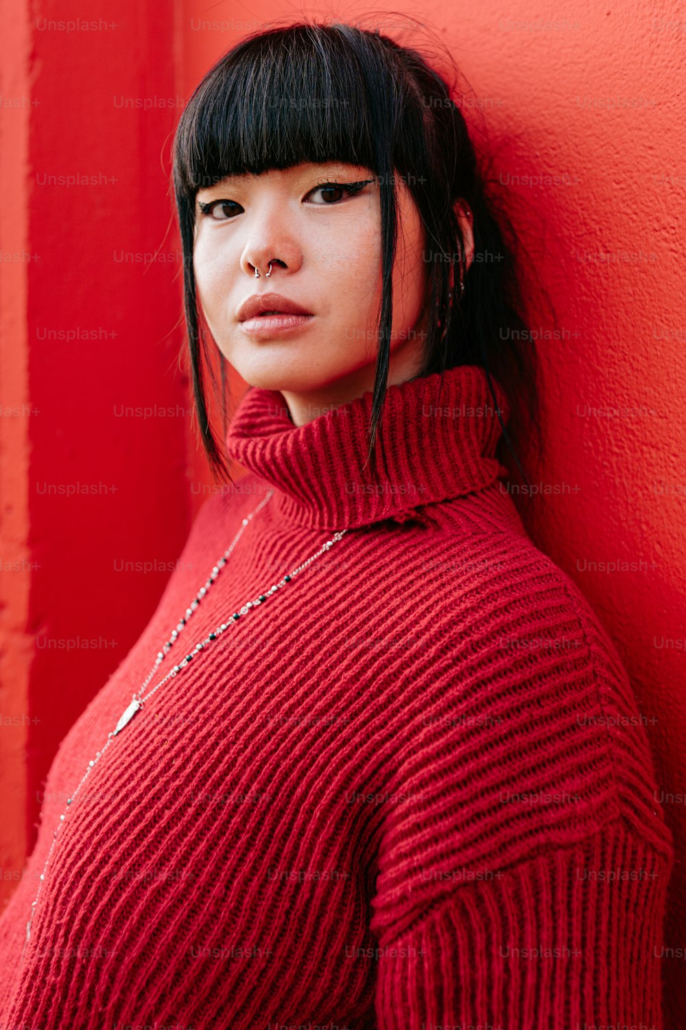 a woman in a red sweater leaning against a red wall