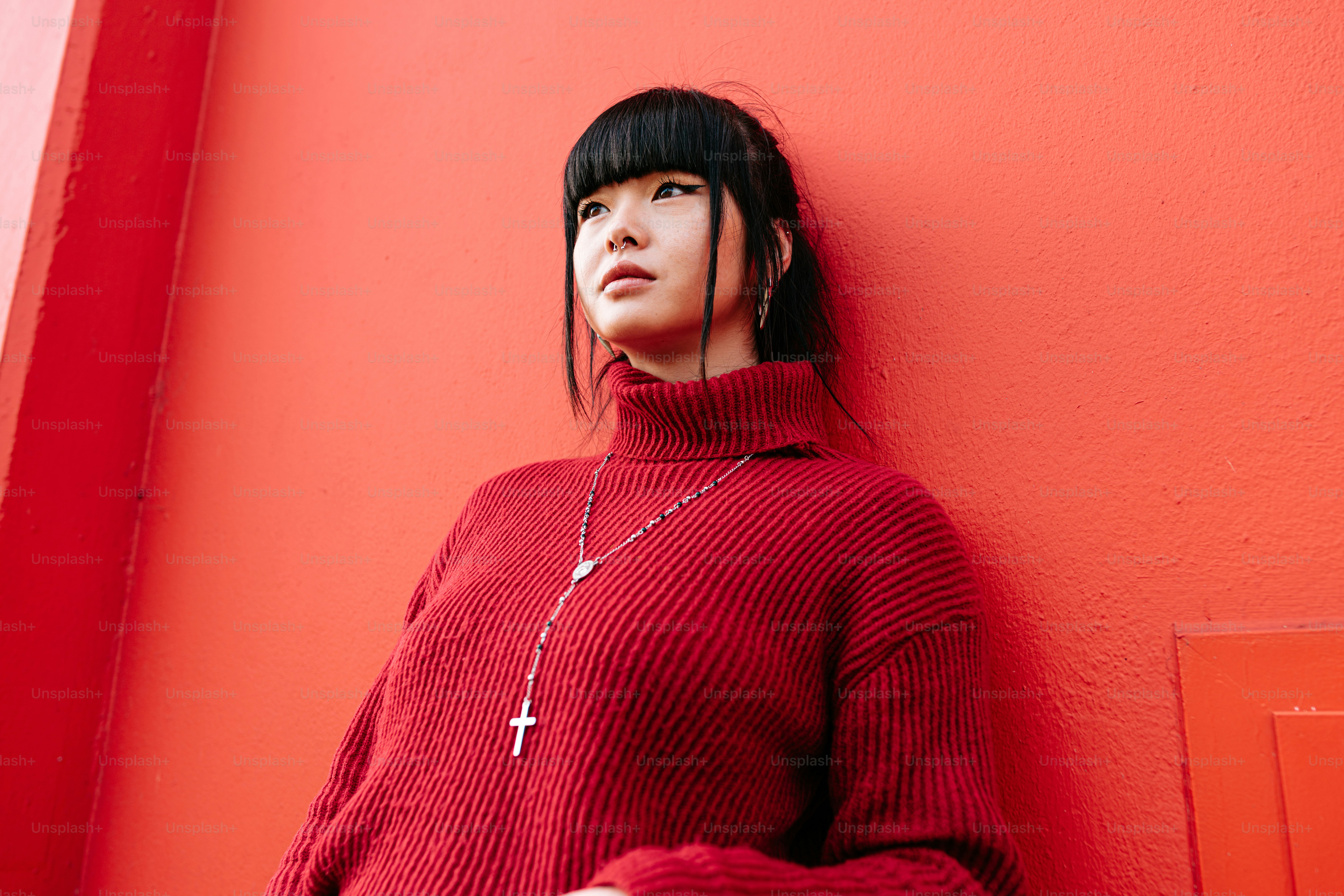 a woman in a red sweater leaning against a red wall