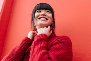 Une femme sourit en s’appuyant contre un mur rouge