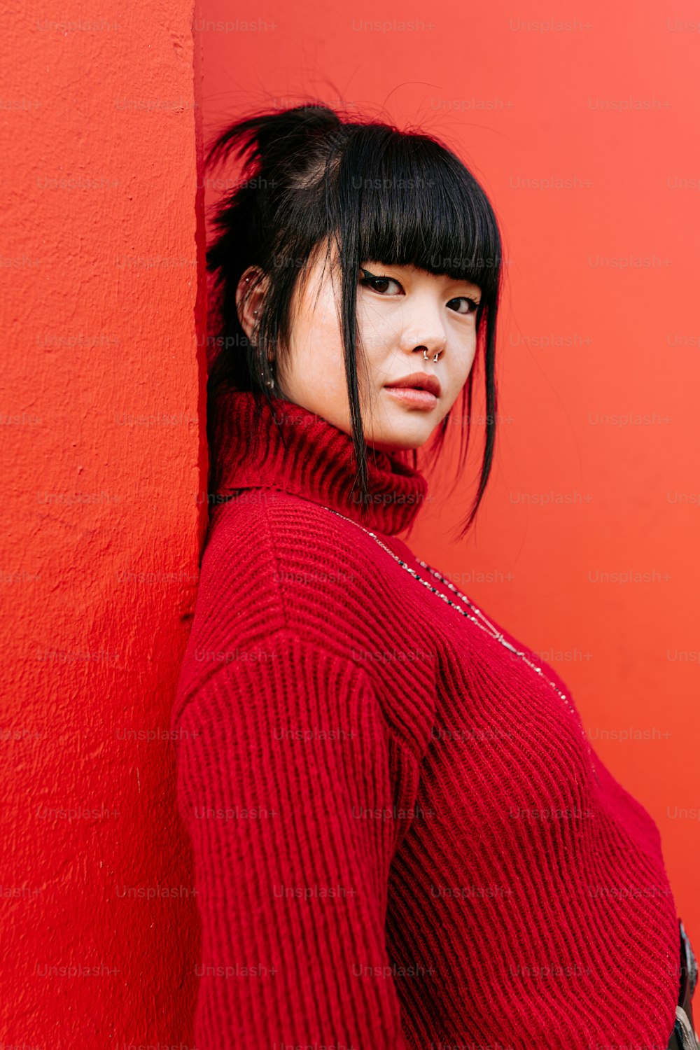 una mujer con un suéter rojo apoyada contra una pared roja