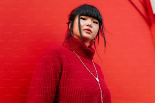 赤いセーターを着た女性が赤い壁を背景に立っている