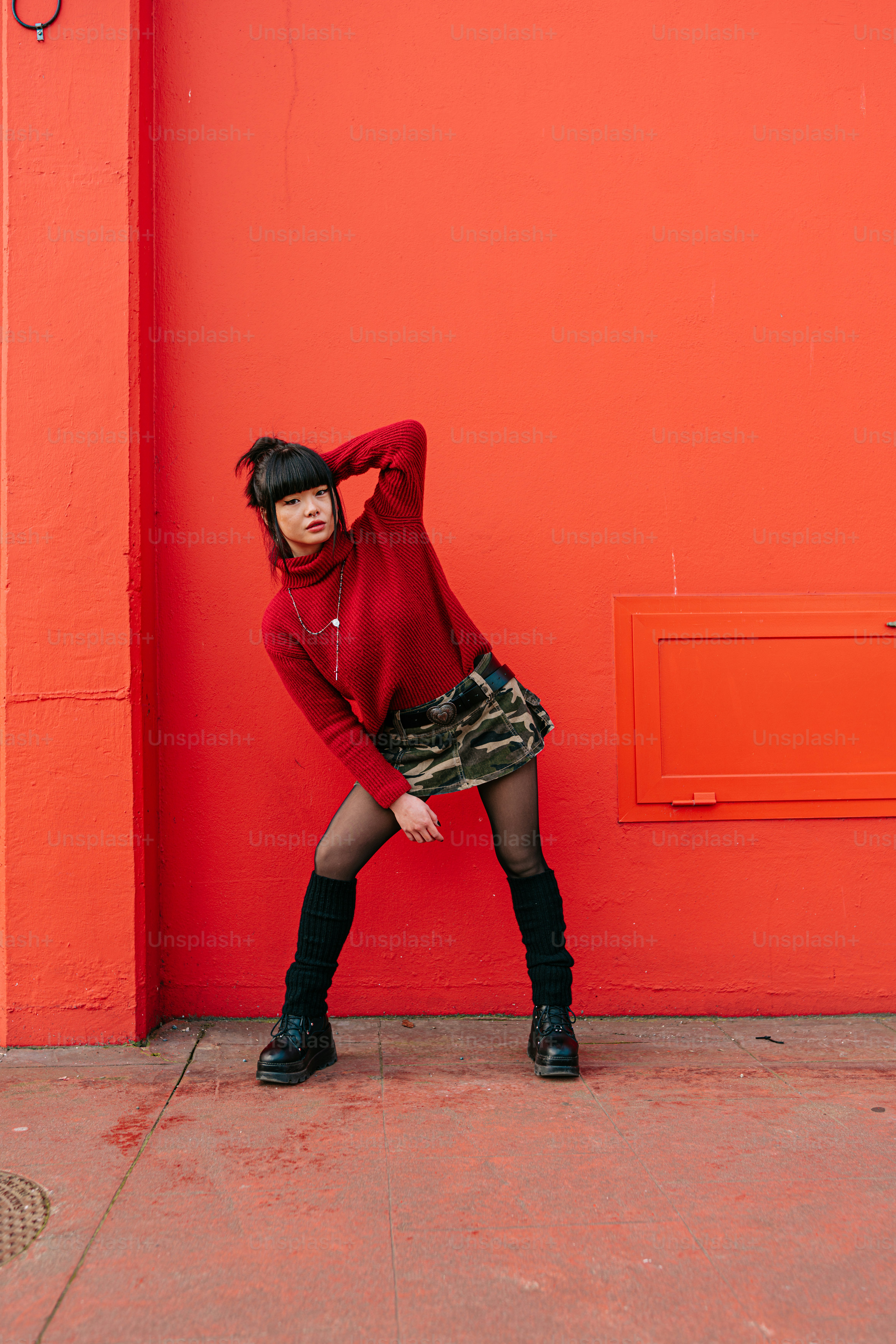 A woman leaning against a red wall with her hand on her head photo ...
