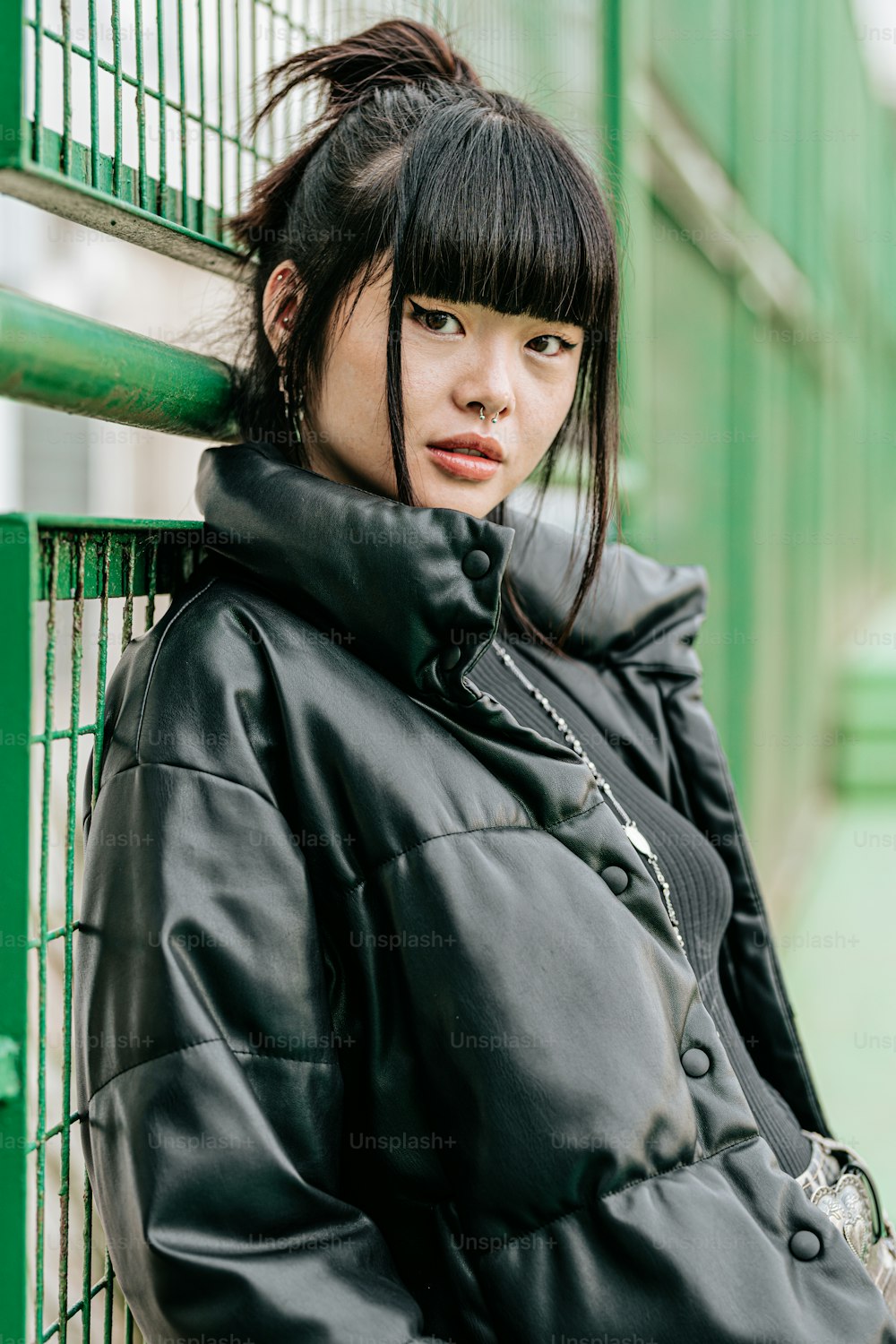 uma mulher com uma jaqueta preta encostada em uma cerca verde
