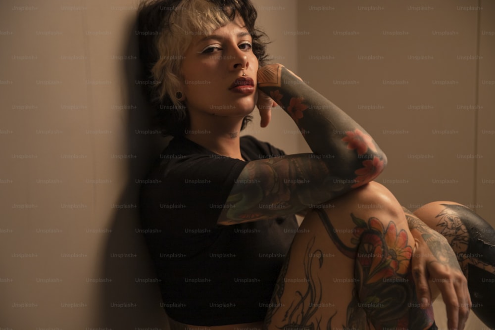 a woman with tattoos leaning against a wall