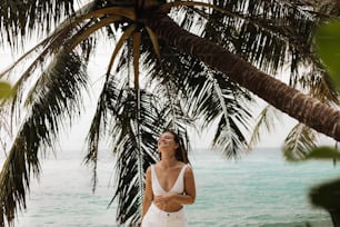 a woman standing under a palm tree next to the ocean