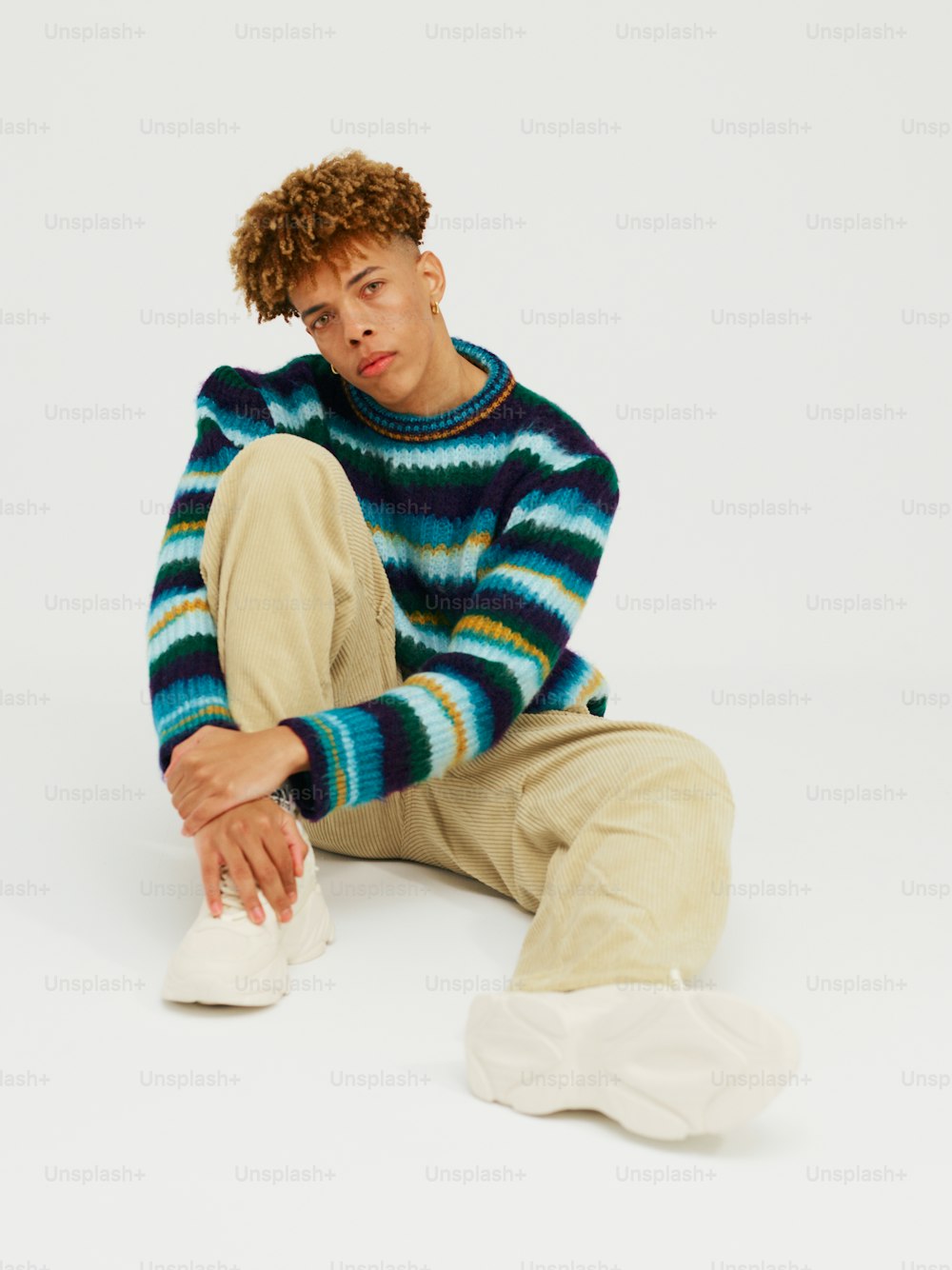 a man sitting on the ground wearing a sweater and pants