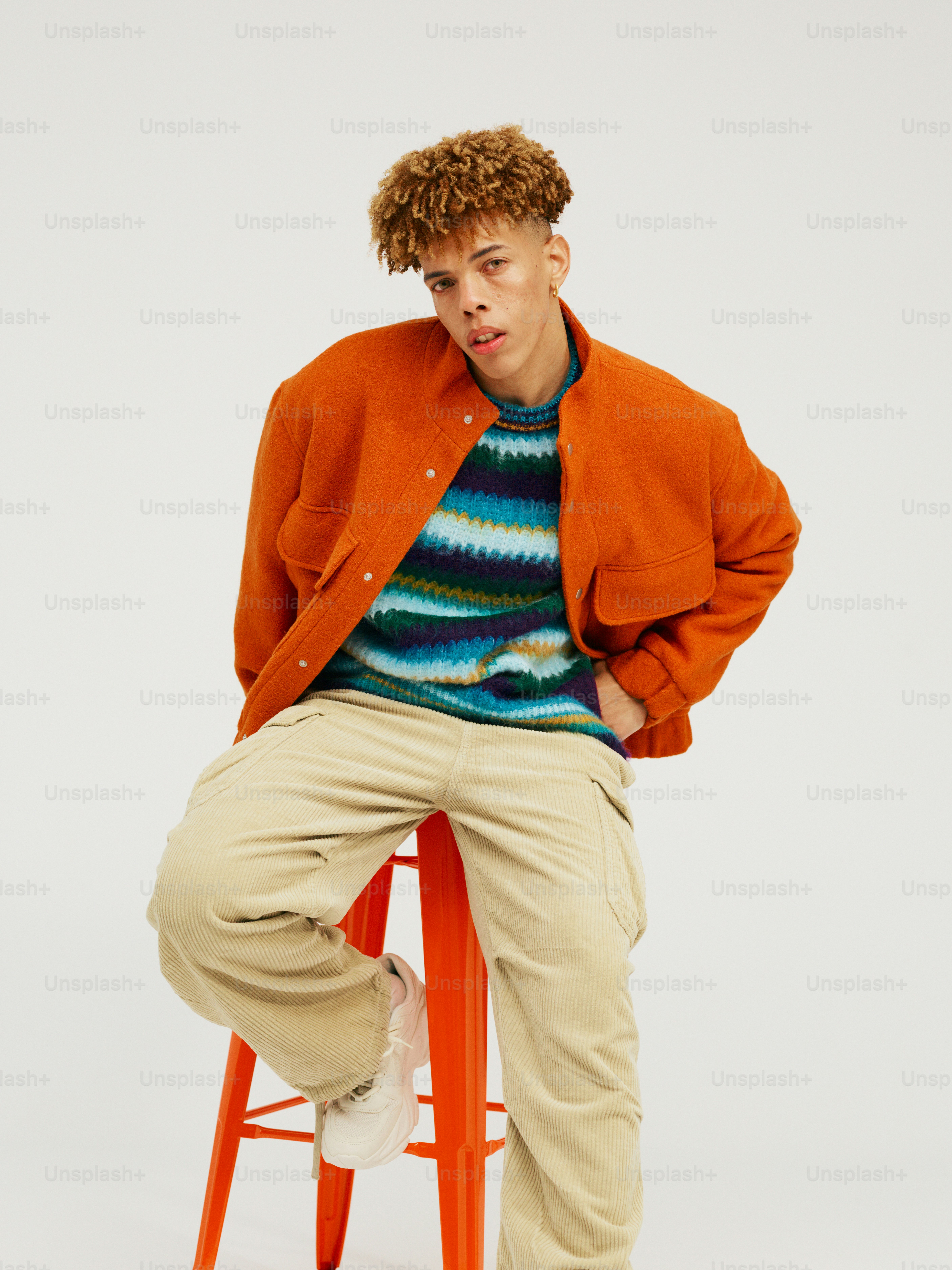 a man sitting on a stool with his hands in his pockets