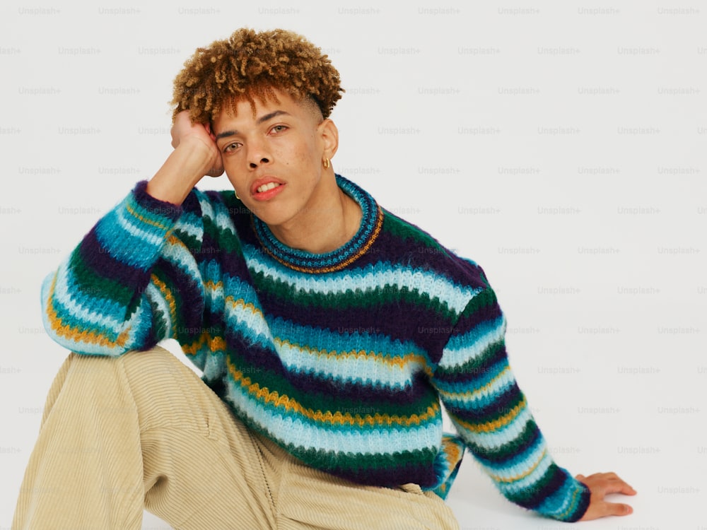a man sitting on the ground wearing a colorful sweater
