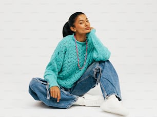 a woman sitting on the ground wearing a sweater and jeans