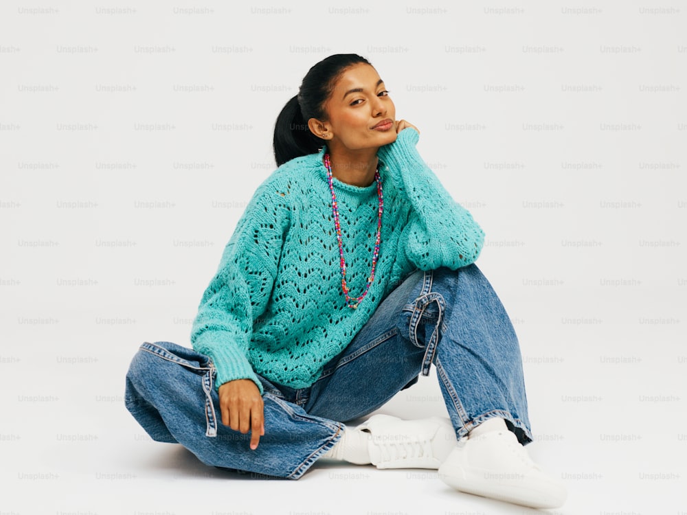 a woman sitting on the ground wearing a sweater and jeans