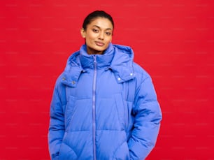 a woman in a blue puffy jacket standing in front of a red background