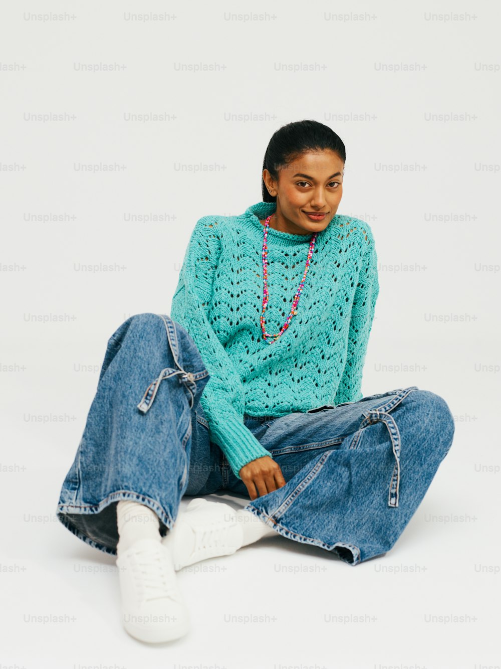 a woman sitting on the ground wearing a blue sweater and jeans