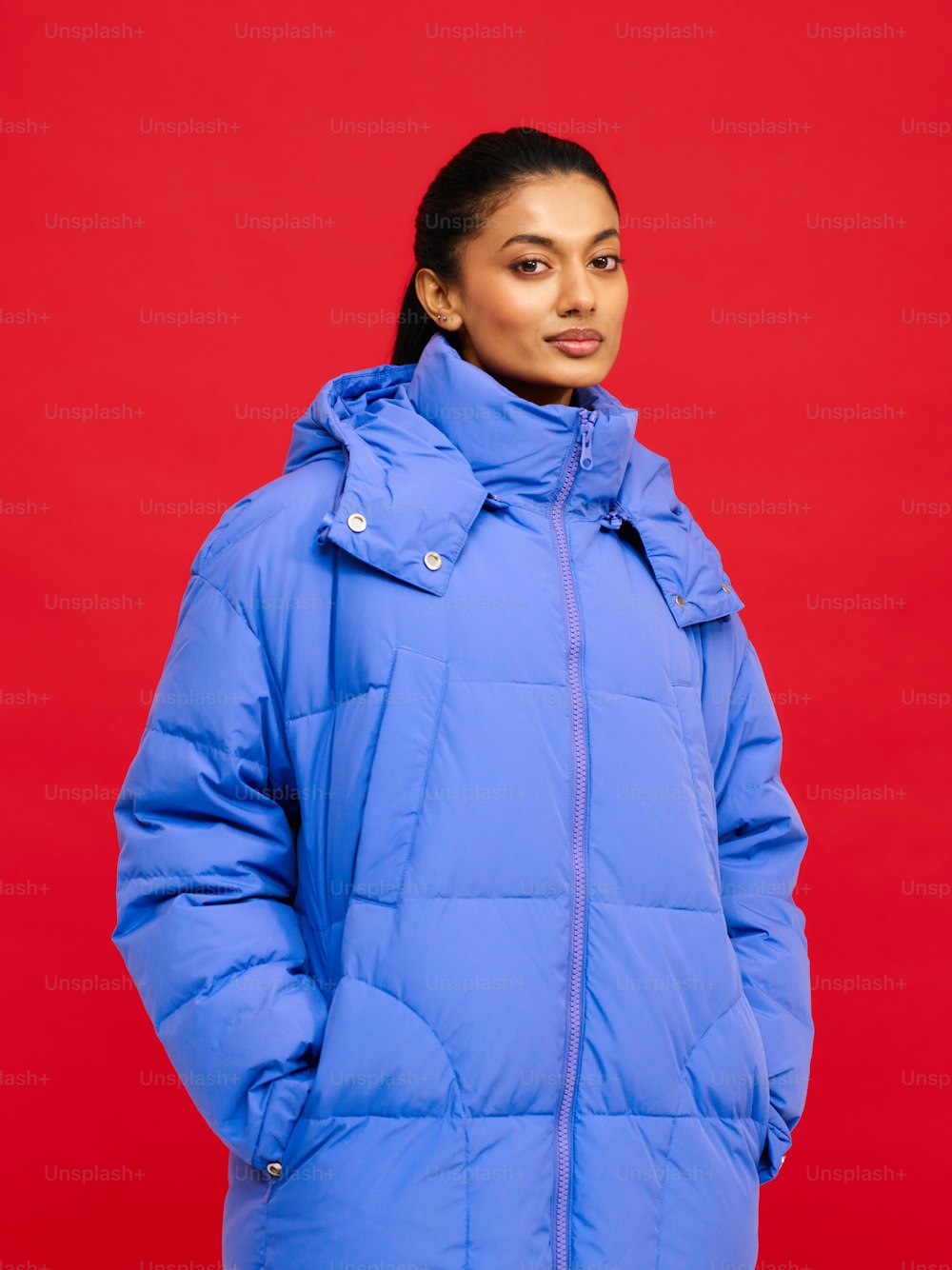 a woman in a blue puffy jacket standing in front of a red background