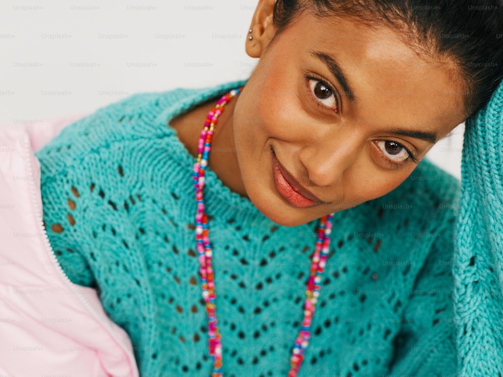 a young woman wearing a blue sweater and a pink necklace
