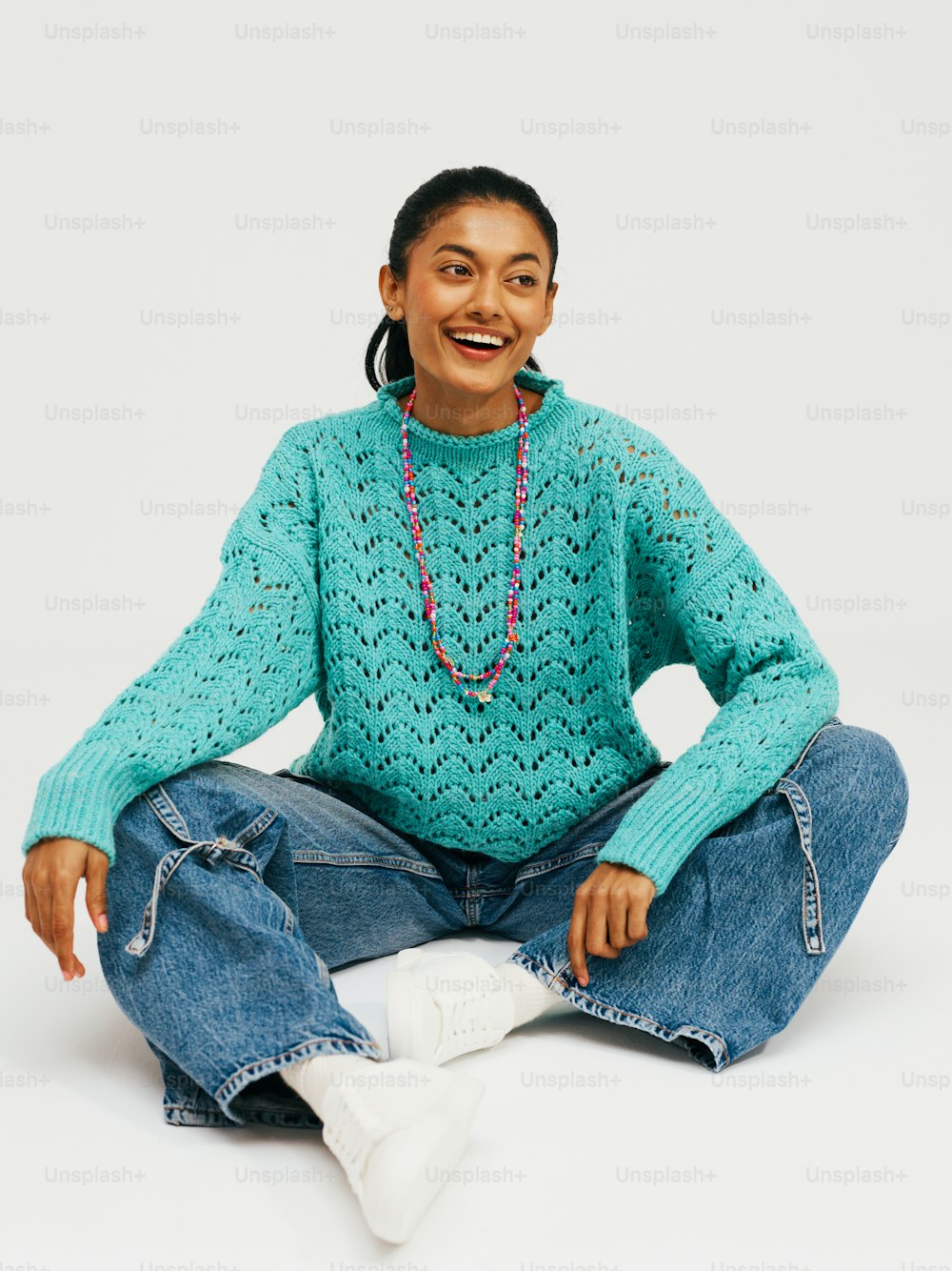 a woman sitting on the floor wearing a blue sweater and jeans