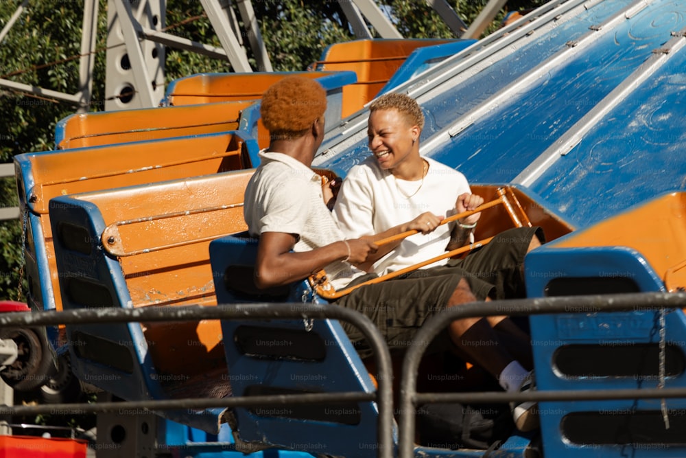 a couple of men sitting on top of a blue and orange bench