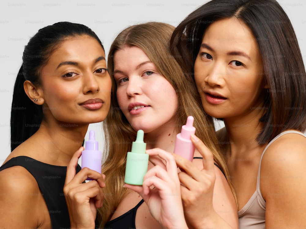 three young women are holding small bottles of lip balm