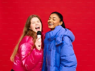 two women are laughing while one of them is holding a microphone