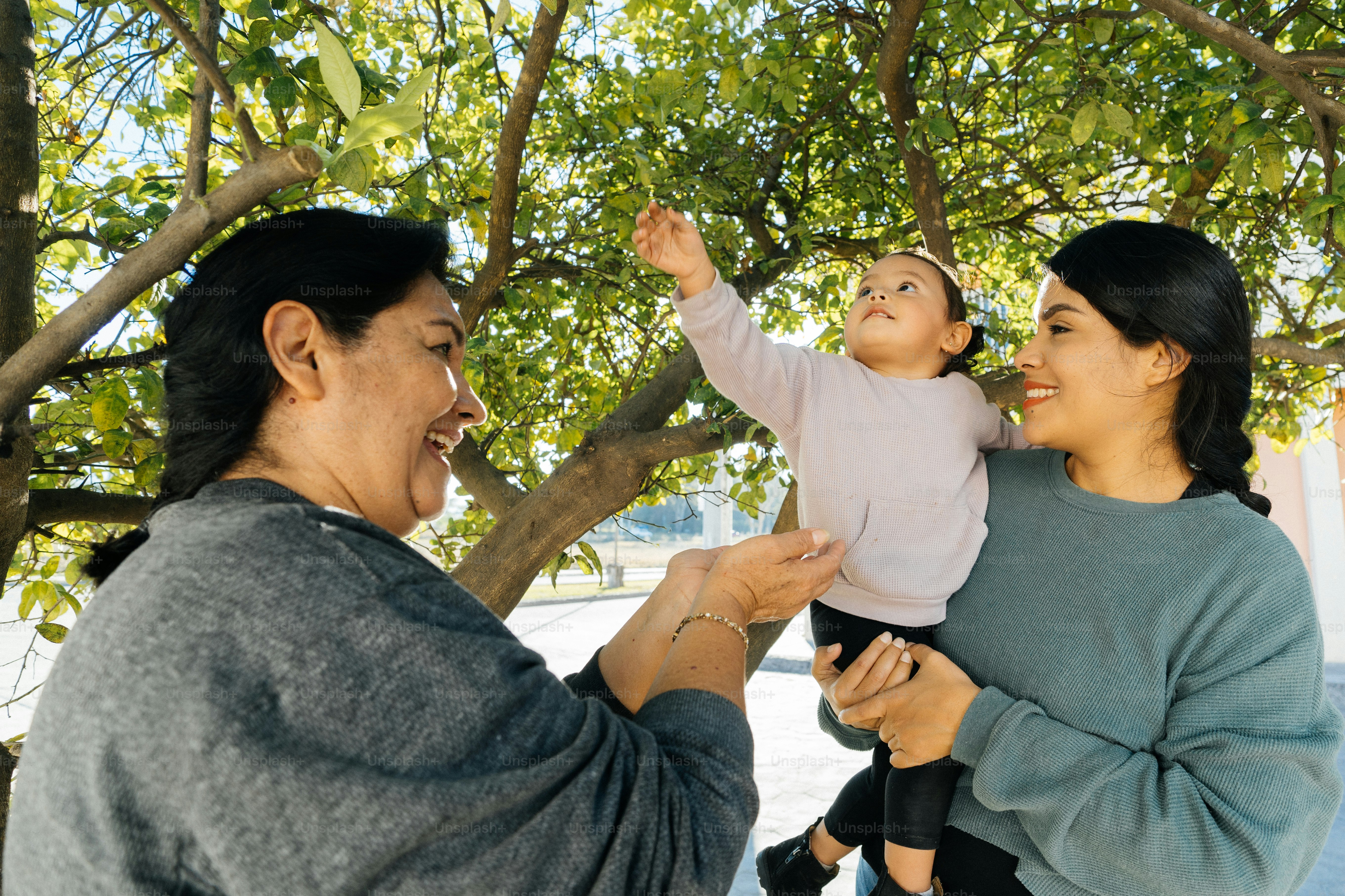 a woman holding a baby up to a tree