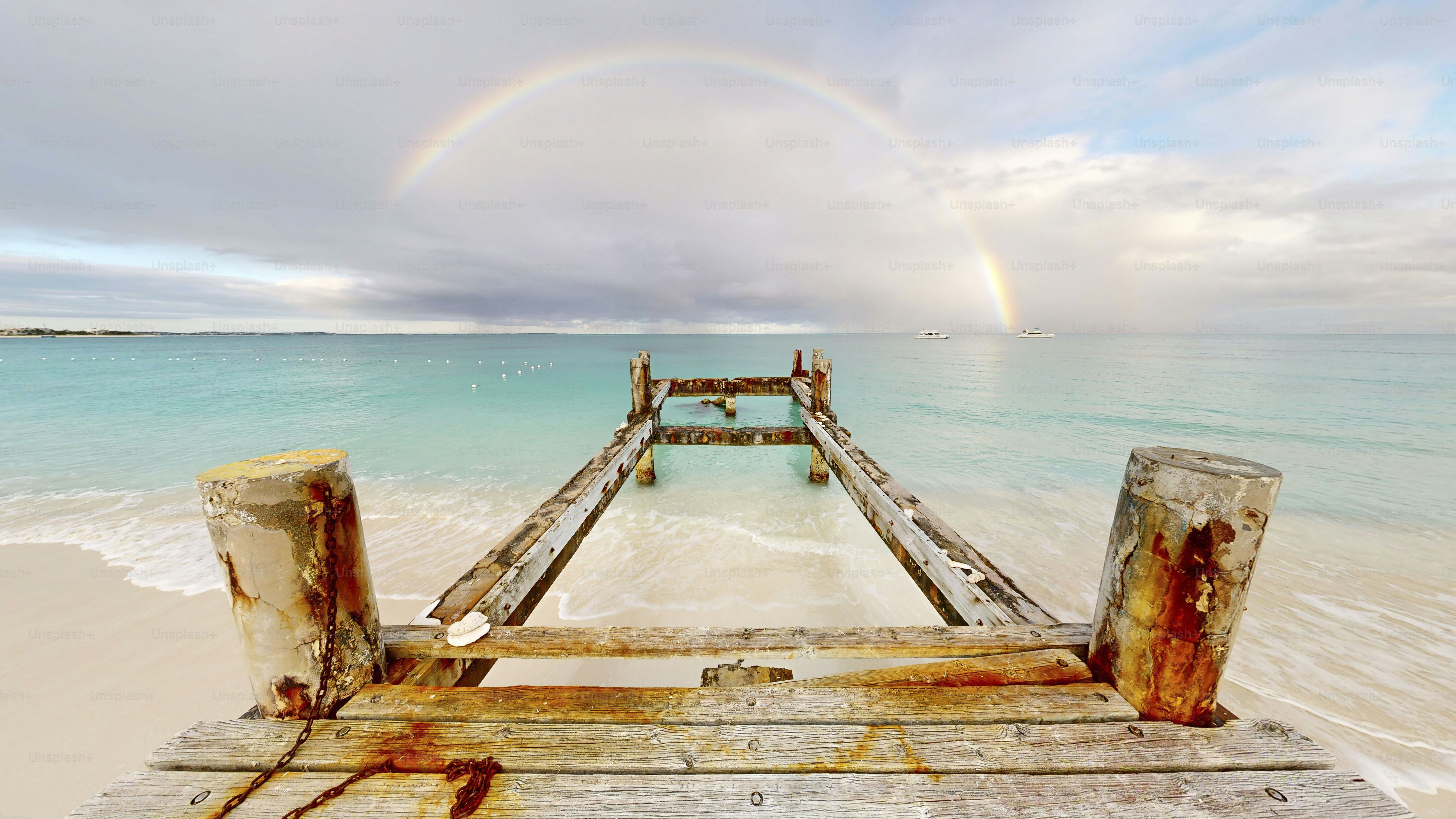 Old wooden pier on a beach with a rainbow overhead