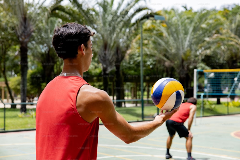 a man in a red shirt is holding a volleyball