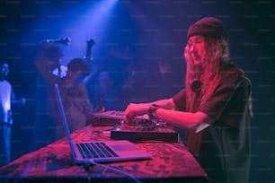 a man with long hair standing in front of a laptop