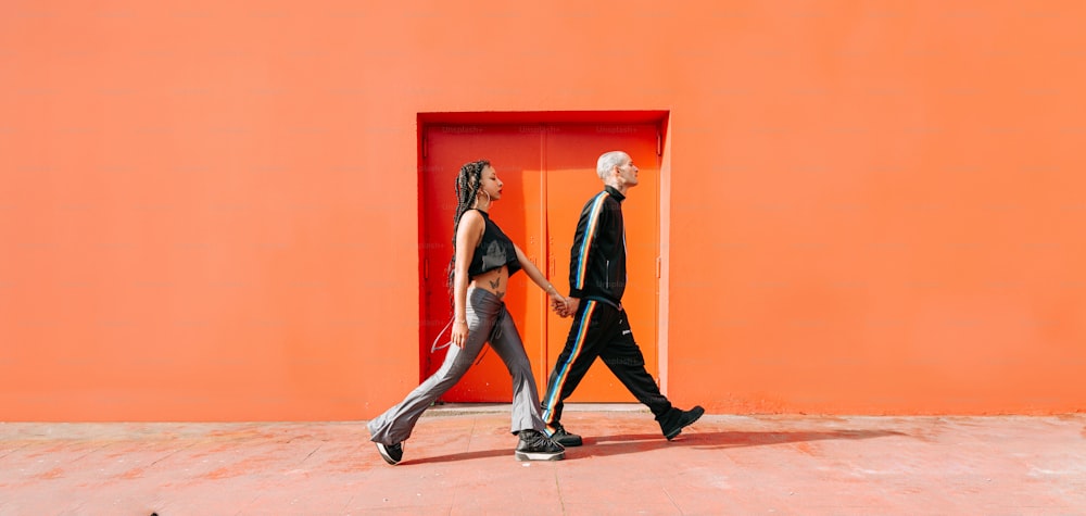 a man and a woman walking in front of an orange wall