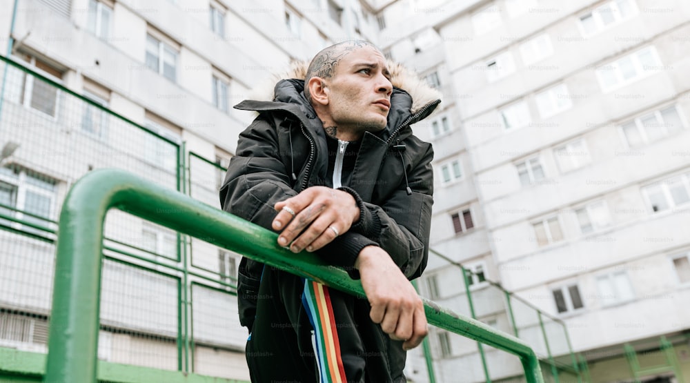 a man in a black jacket leaning on a green rail