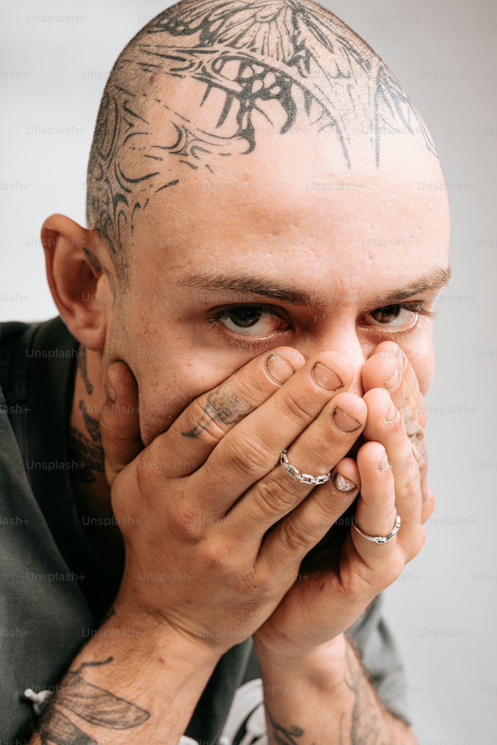 um homem com tatuagens cobrindo o rosto com as mãos