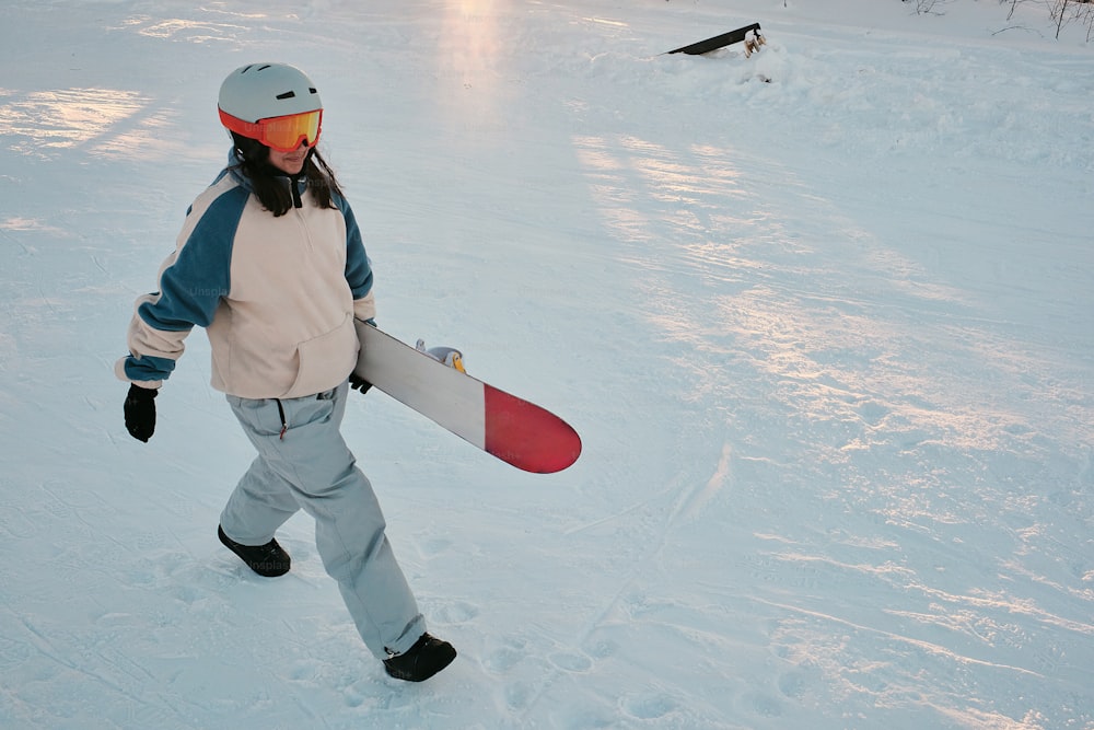 uma pessoa andando na neve carregando uma prancha de snowboard