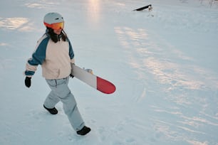 Una persona caminando en la nieve llevando una tabla de snowboard