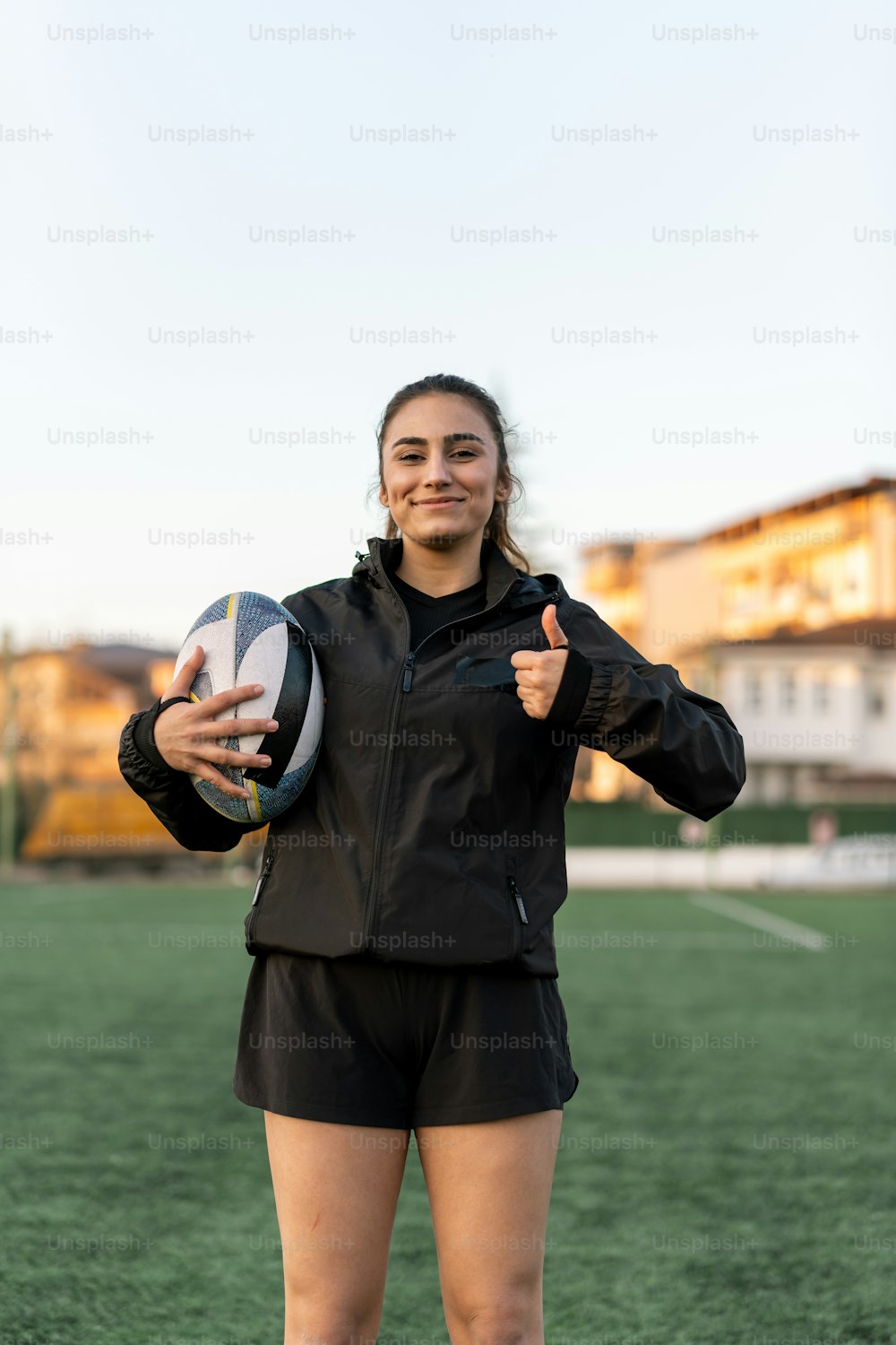 a woman holding a rugby ball and giving a thumbs up
