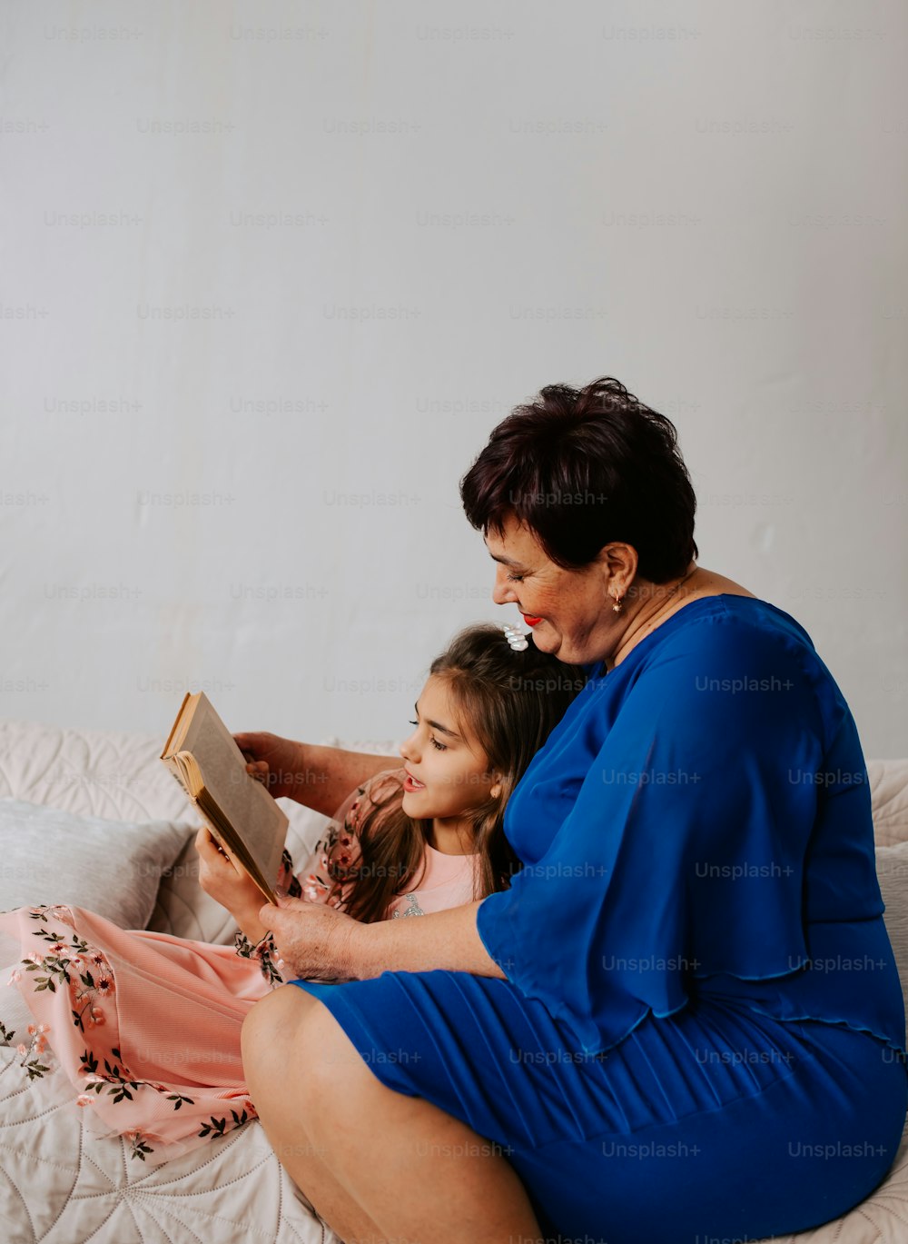 a woman sitting on a bed reading a book to a little girl