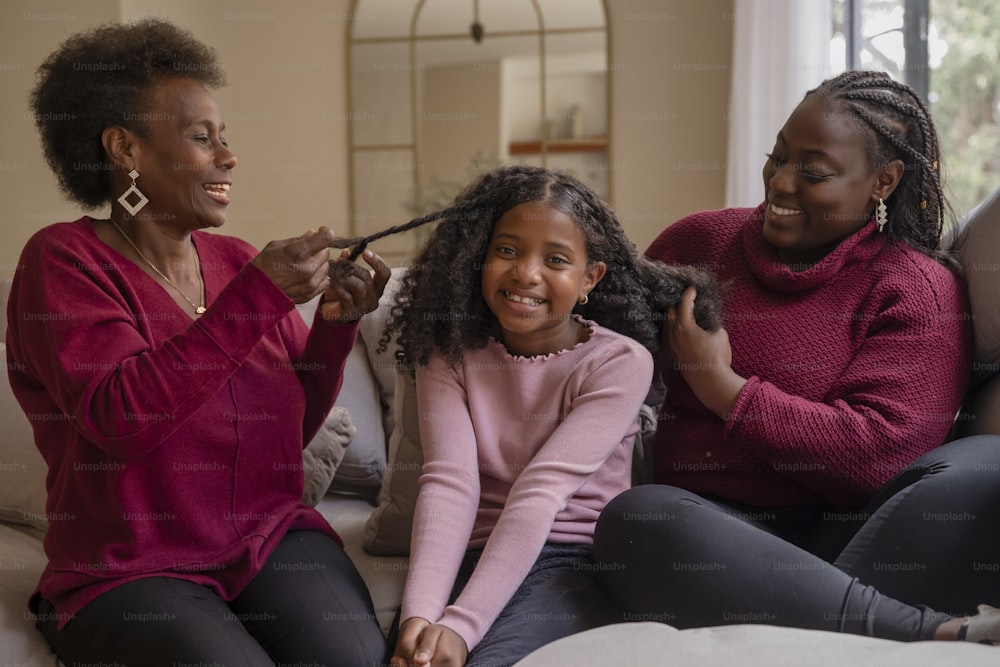 a woman and two girls sitting on a couch brushing their hair